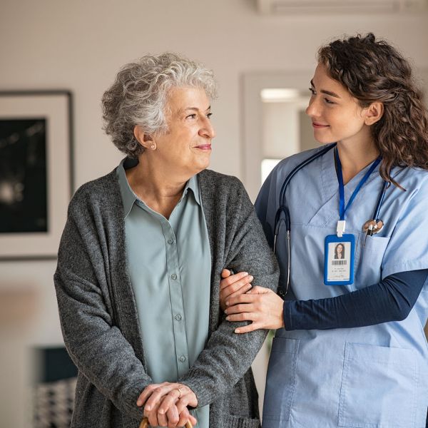 Young caregiver helping senior woman walking — nursing home context